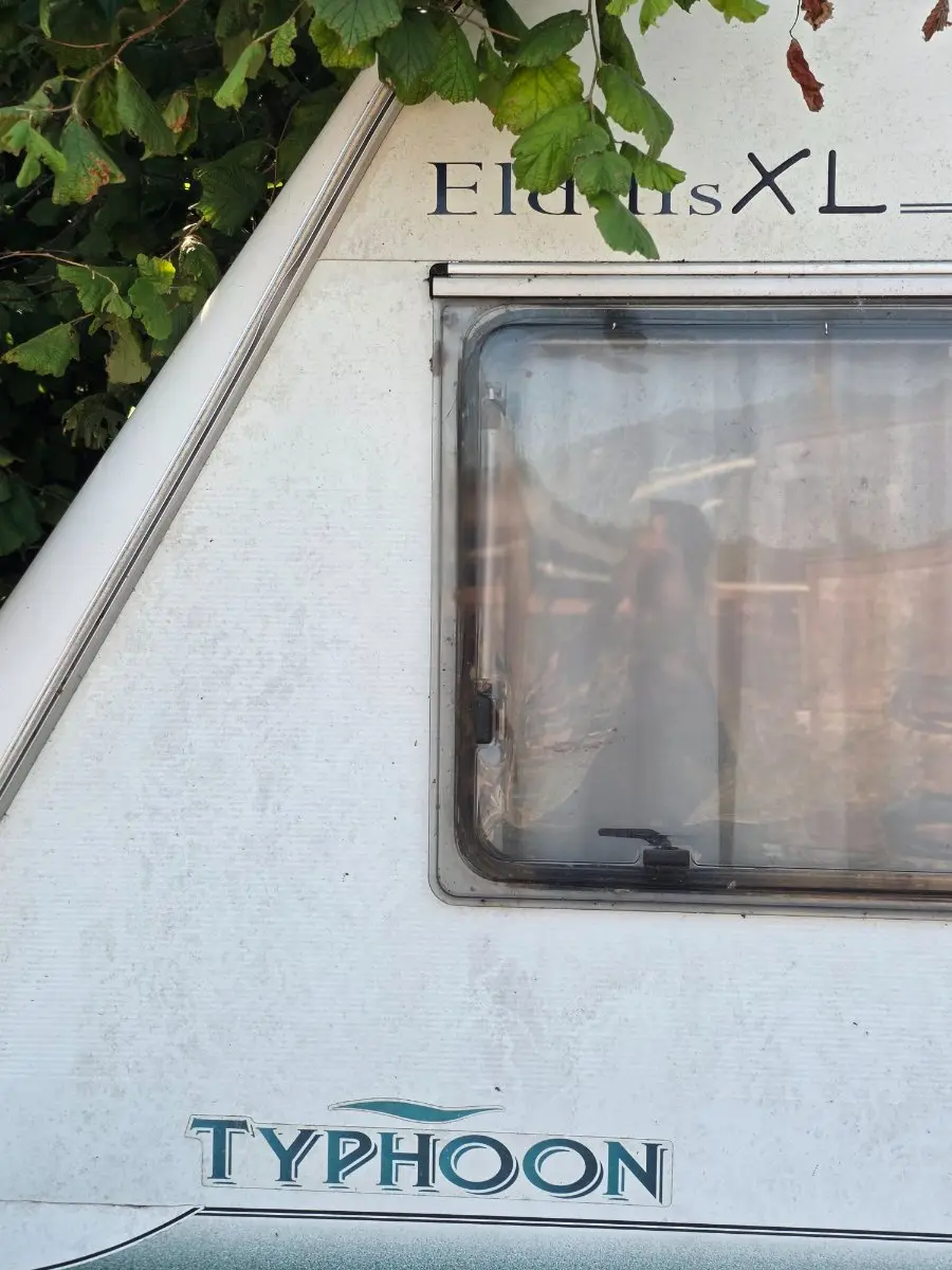 Close-up of an Elddis Typhoon front panel, the badge still crisp but the panel chalky and the window misted from the inside, age and condition rather than the name setting the value