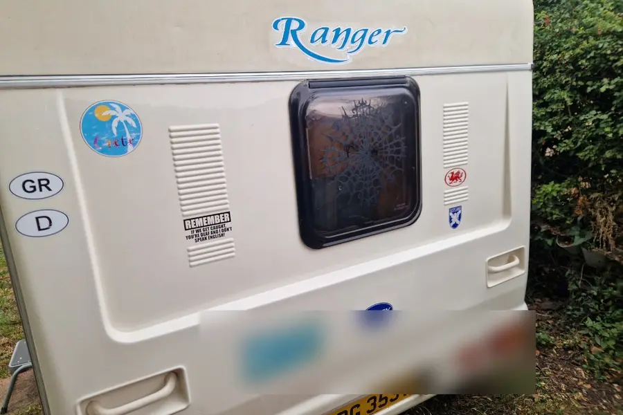 Rear panel of a touring caravan carrying travel stickers and a mirrored registration plate, the detail that decides whether a V5C has to be surrendered
