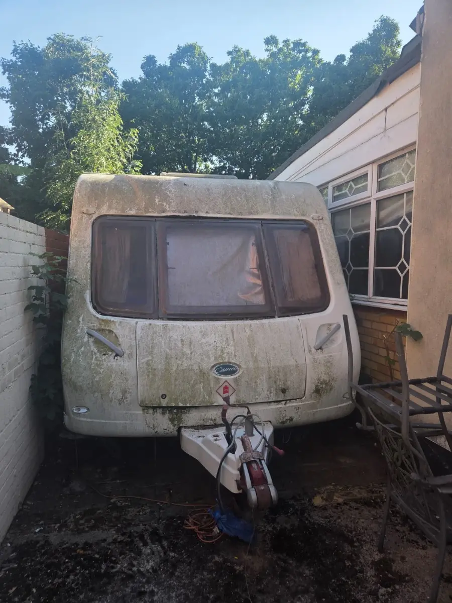 Touring caravan streaked green with algae, jammed between a bungalow wall and a boundary wall with barely a body-width of clearance either side — the access problem a Slough collection is quoted around