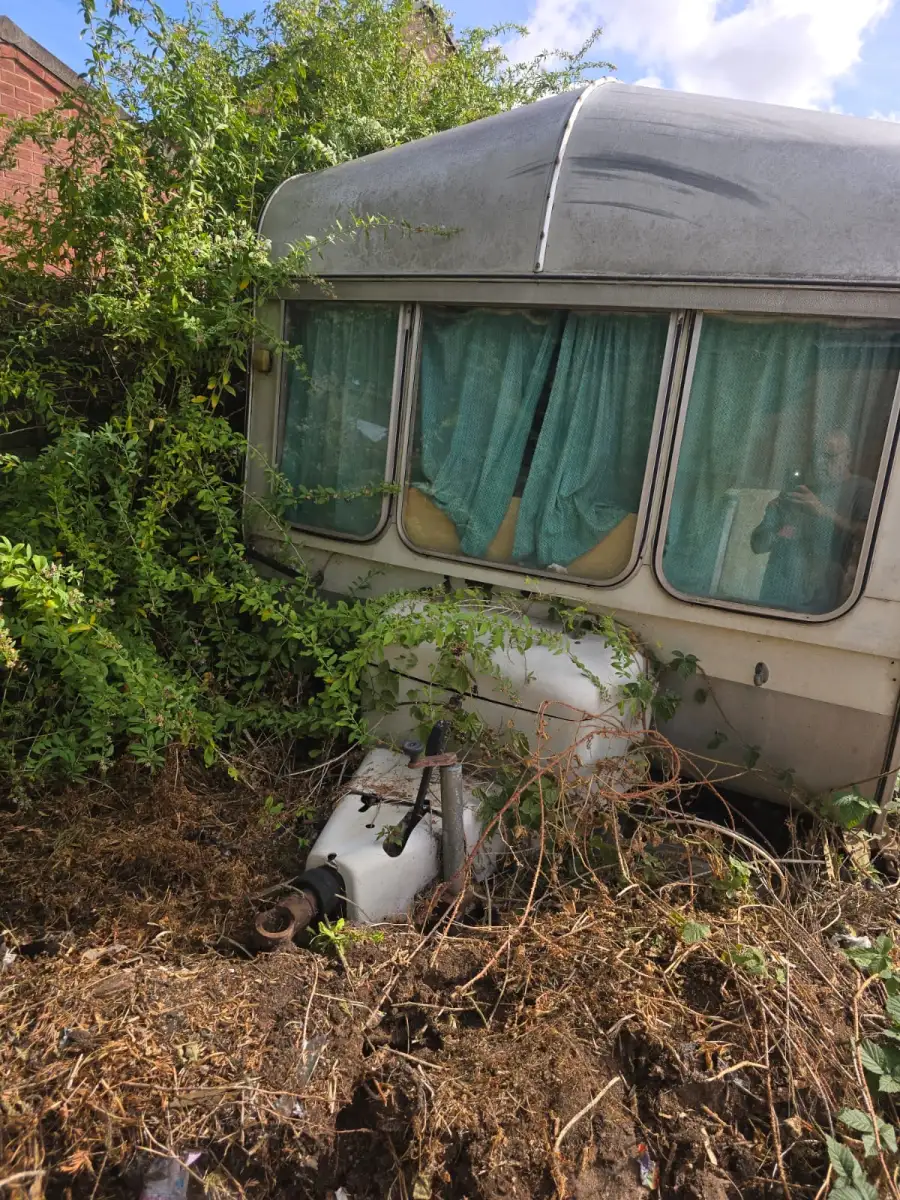 Touring caravan swallowed by brambles with the hitch buried, the overgrown access that shapes collection planning around Basingstoke