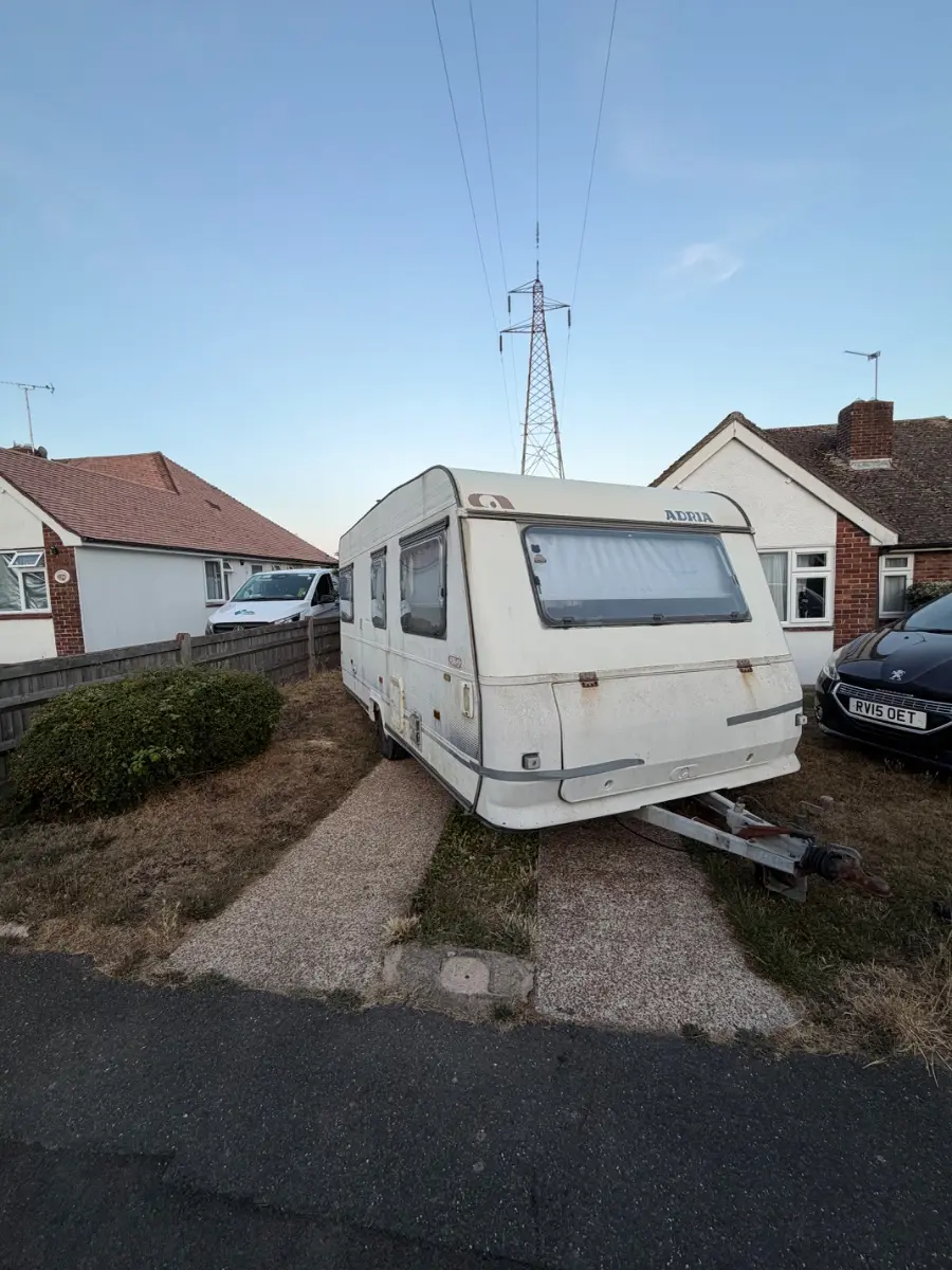 Touring caravan hitched and standing on a narrow driveway between two bungalows, the tight access that decides whether a tourer can be towed out whole