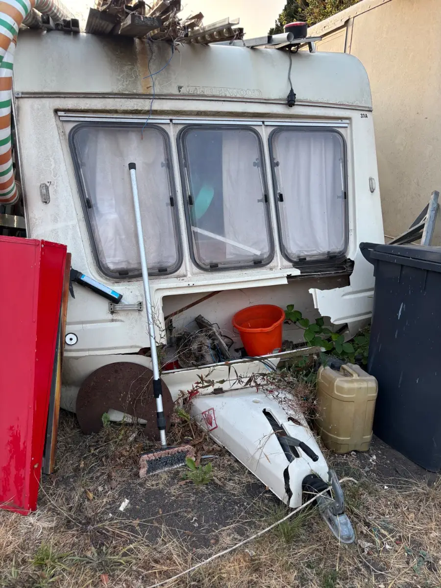 Caravan with its front panel broken open and the jockey wheel lying detached in the grass among loose fittings, a mix of timber, metal and plastic no household tip will take