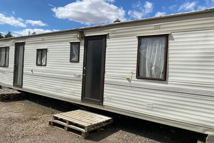 Long white static caravan on hardstanding with a wooden pallet doing duty as a step, the kind of unit that needs dismantling on site rather than towing away
