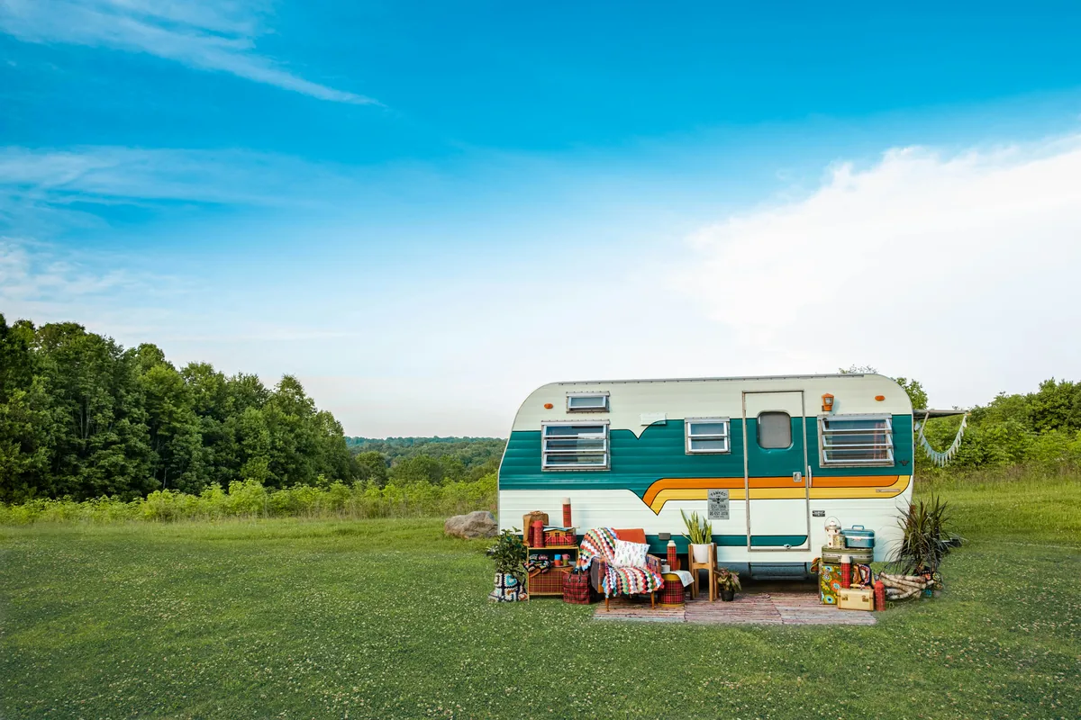 Older touring caravan standing alone on open grass with trees behind, typical of a caravan left on a pitch or paddock near Dunstable