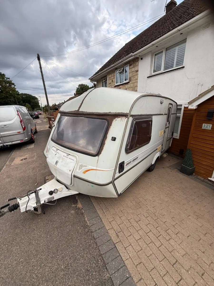 White touring caravan standing on a house driveway, complete and on its wheels, the kind of collection we arrange from where a caravan is already kept