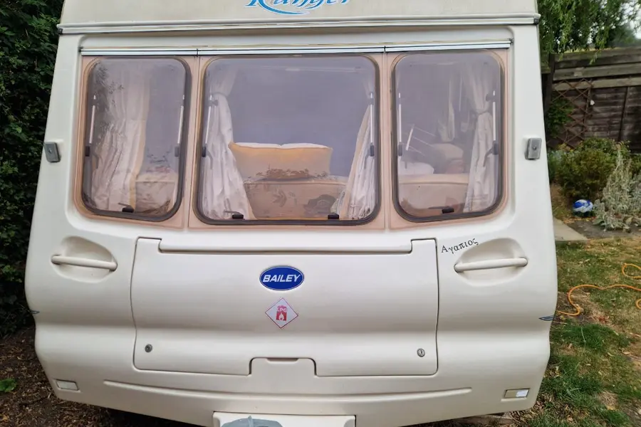 Front end of a touring caravan on grass, curtains drawn across its three front windows — far taller and wider than the trailer a household waste site will accept