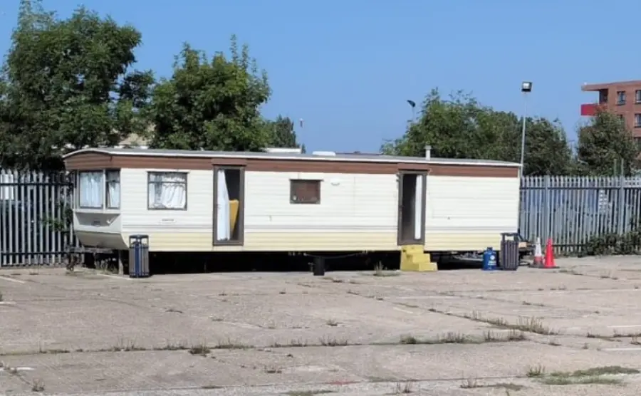 Static caravan standing on a fenced hardstanding yard with its steps at the door, a unit that has to be dismantled where it sits rather than towed out
