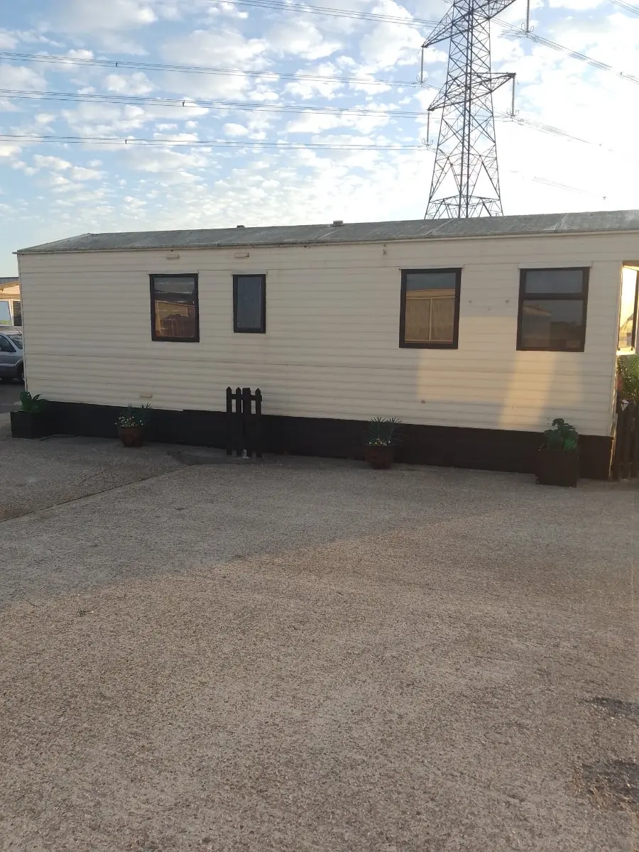 Long side view of a weathered cream static caravan on a gravel pitch, size and access being what set a static dismantling price