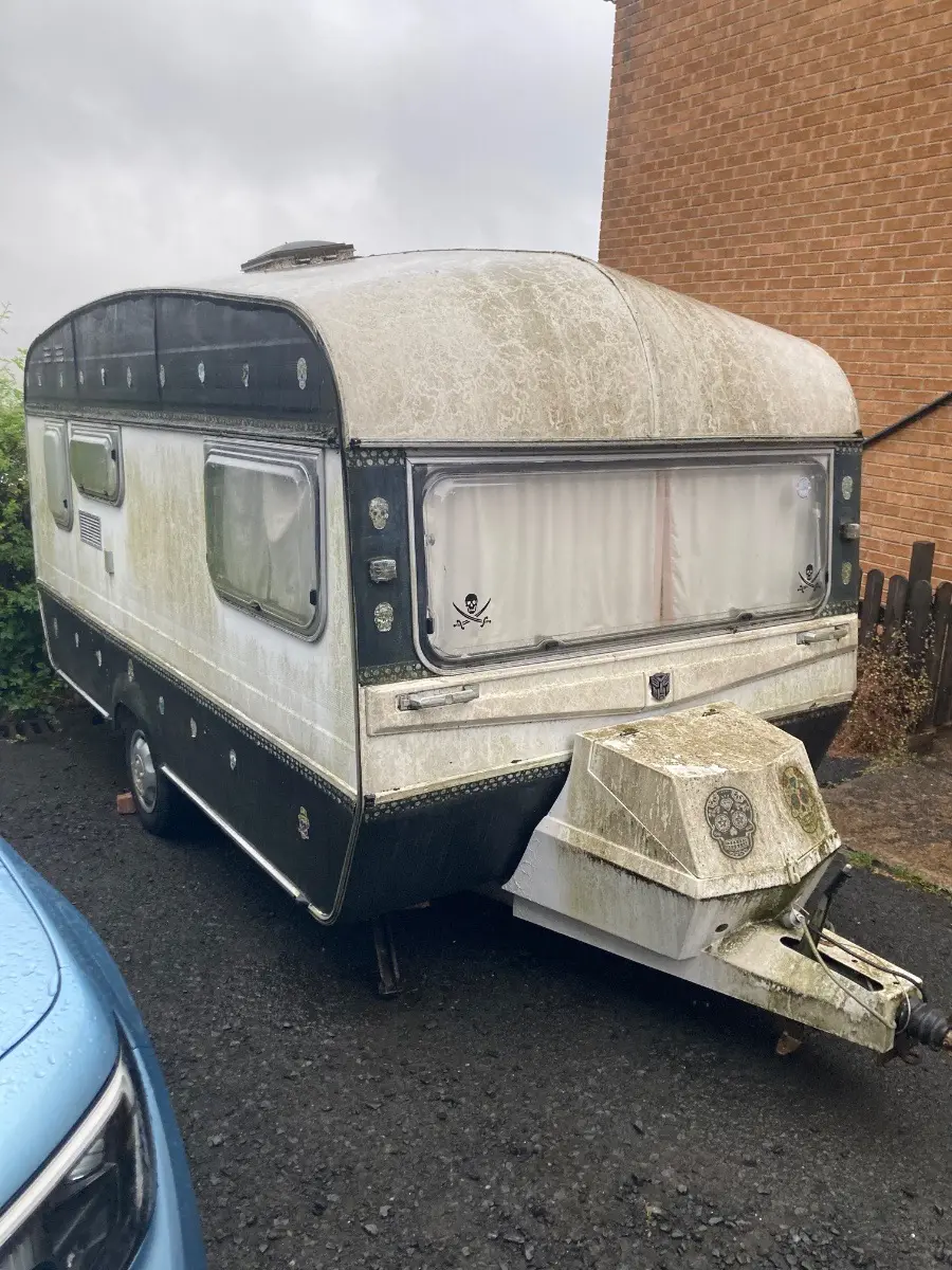Vintage touring caravan streaked green with algae, well past any salvage value and still a priced Basingstoke removal