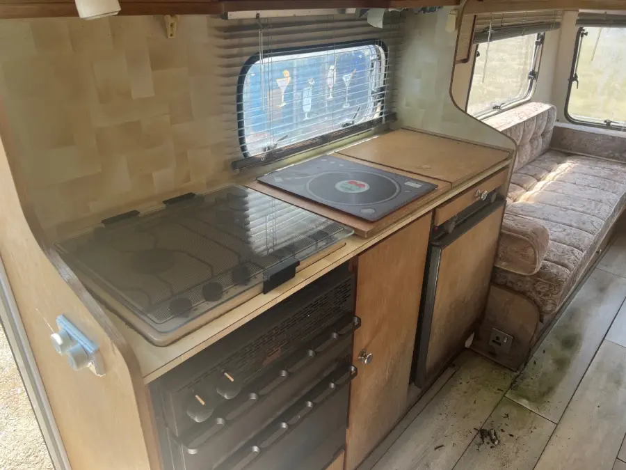 Grubby caravan interior with a timber-faced kitchen unit, fabric bench seat and a debris-strewn floor — the mix of timber, foam and plastic that stops a shredder taking a caravan