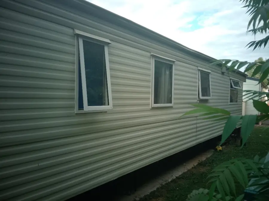 Long flank of a static caravan with greenery grown up tight against the cladding, the kind of overgrown plot access we check before booking a Bedfordshire collection