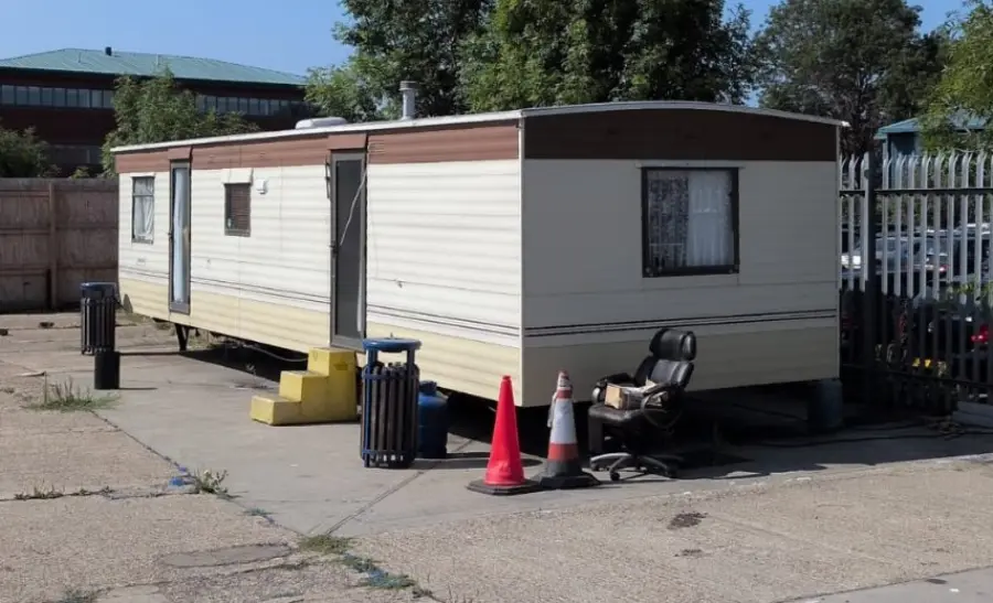 Static caravan seen along its full flank with cones and clutter at the base, the footprint that has to be planned around on a tight residential plot
