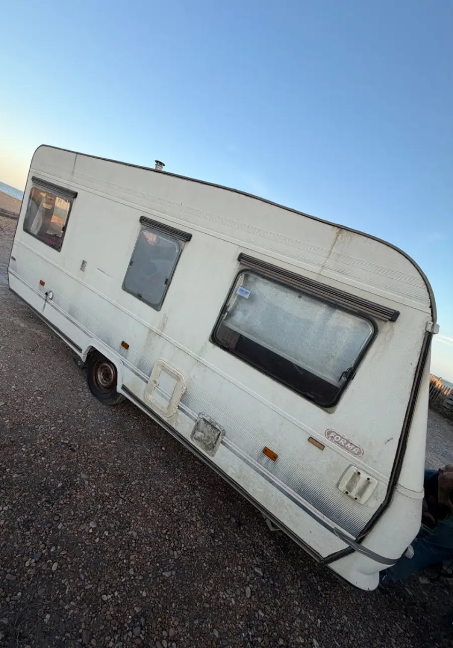 Weathered white touring caravan photographed side-on in low sun, still towable and quoted as a whole-caravan collection