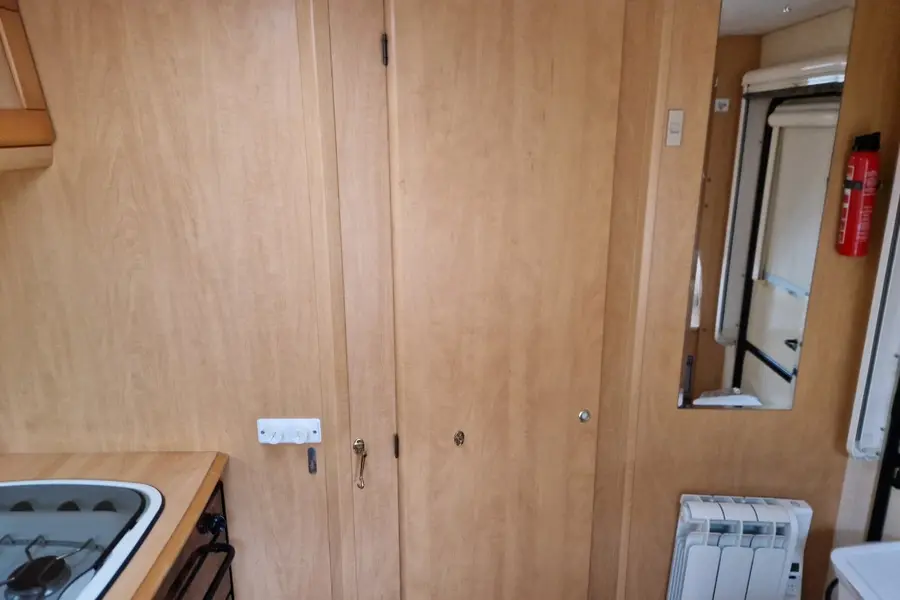 Inside a caravan: pale timber-veneer wardrobe doors and lockers next to a hob and a wall radiator, the mix of timber, plastic and metal that a standard scrap yard cannot process
