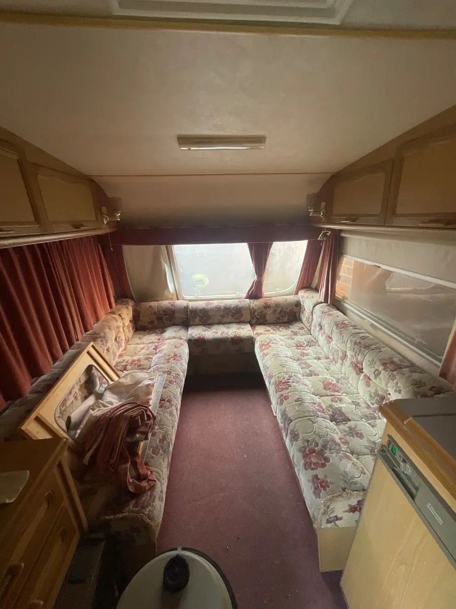 Touring caravan lounge with patterned upholstery and curtains, worn but complete, the sort of used tourer our buying service considers