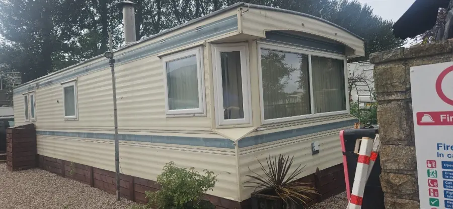Cream and blue static caravan sited end-on beside a boundary wall, ready to be dismantled — the kind of job scheduled into a Bedfordshire collection run