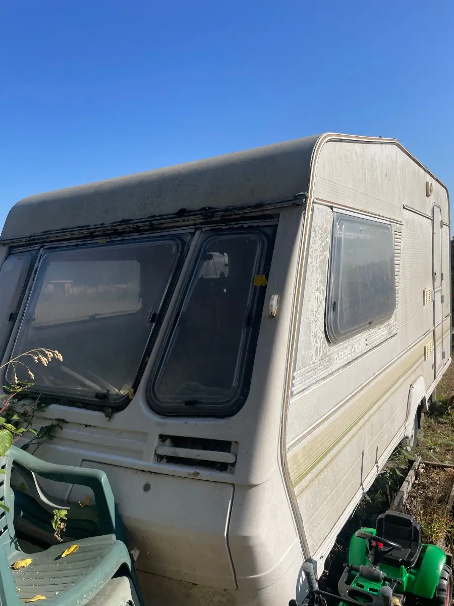 Weathered tourer parked up in a yard with moss along the roof edge and garden chairs stacked against its side, photographed the way we ask owners to photograph theirs