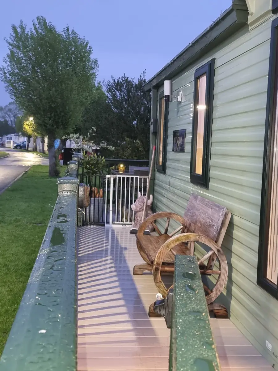 Static caravan on a park pitch at dusk with raised timber decking running along its side and a gravel path beyond — the access a site collection is quoted around