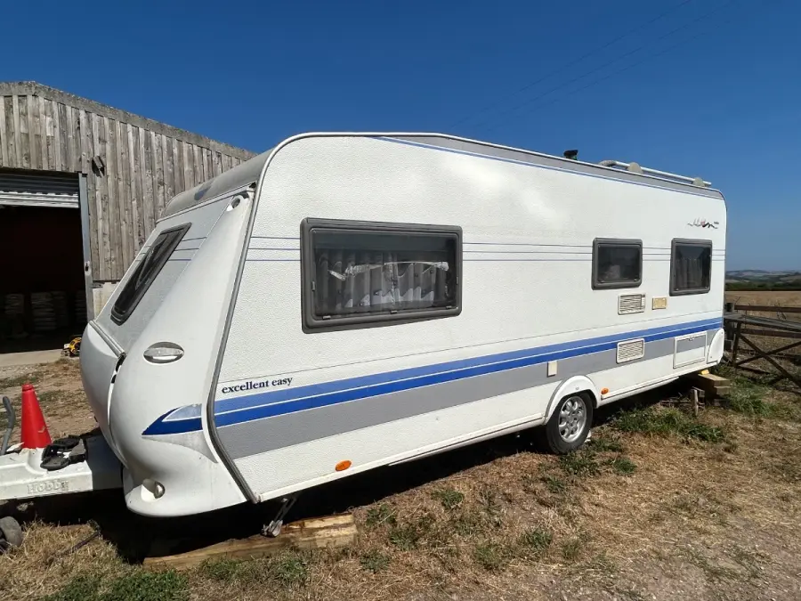 Touring caravan hitched and standing on level ground beside a timber barn, ready for a booked collection