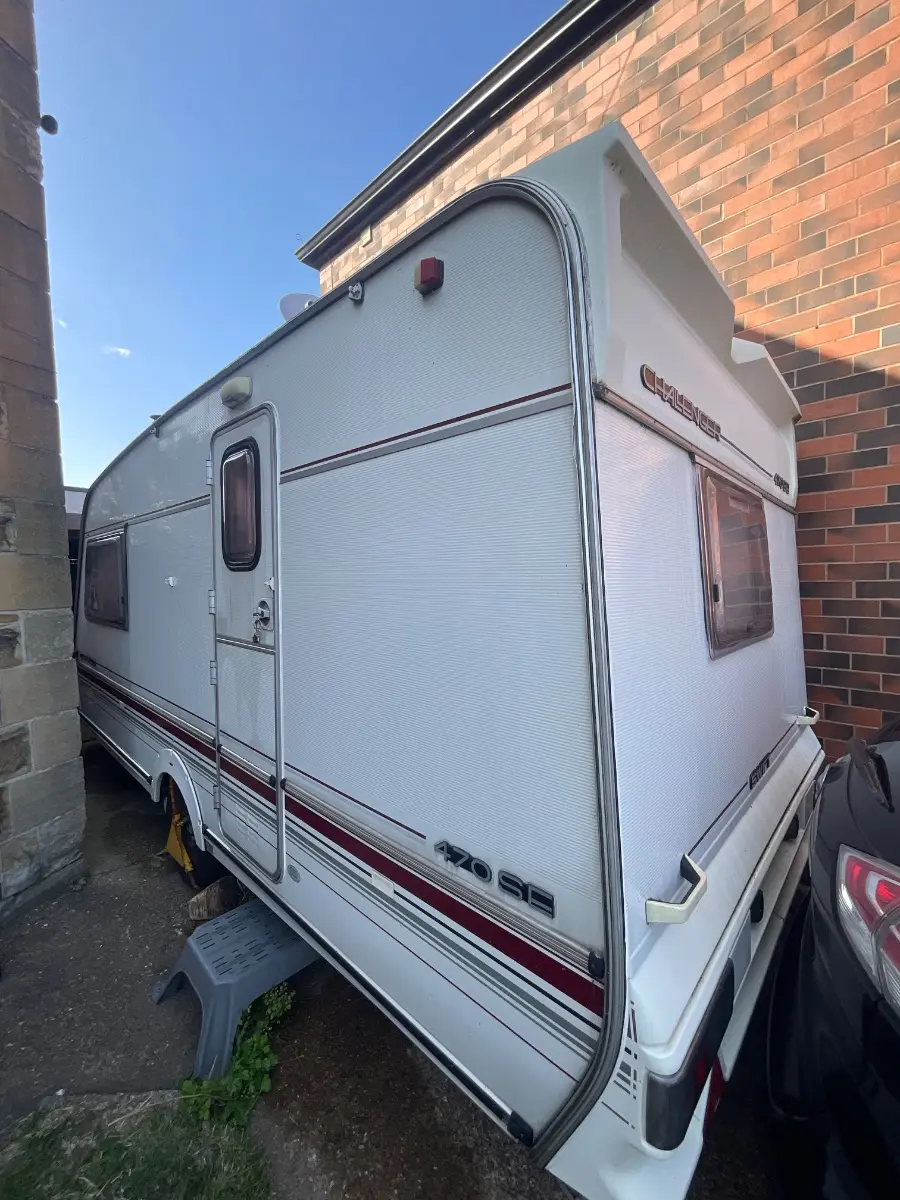 Touring caravan with a maroon stripe parked tight against a red brick house wall on a domestic driveway, a car alongside — typical access on a Berkshire collection