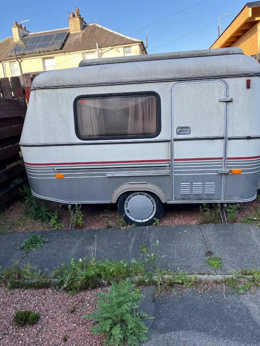 Small 1980s touring caravan left on a house driveway with weeds growing through the paving, the sort of Bedford collection we price from photos