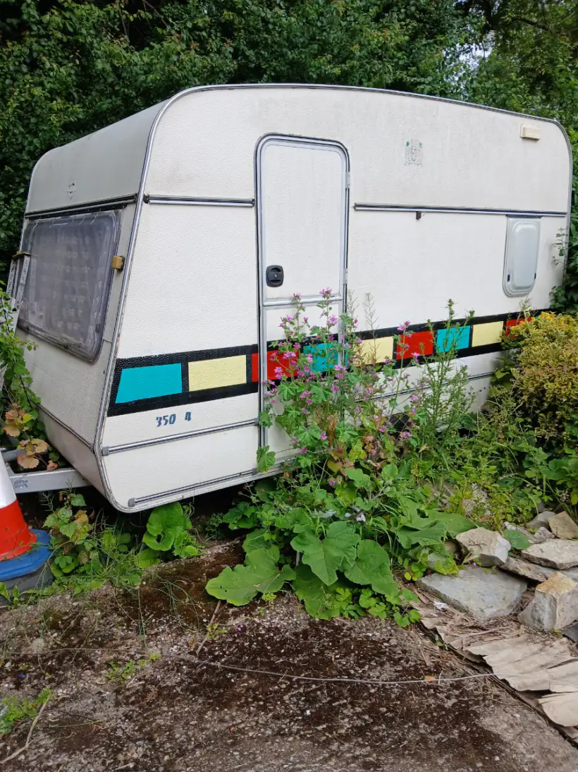 Touring caravan left on a driveway with weeds and flowering plants grown up over the hitch, the point at which an owner starts looking for a collection service