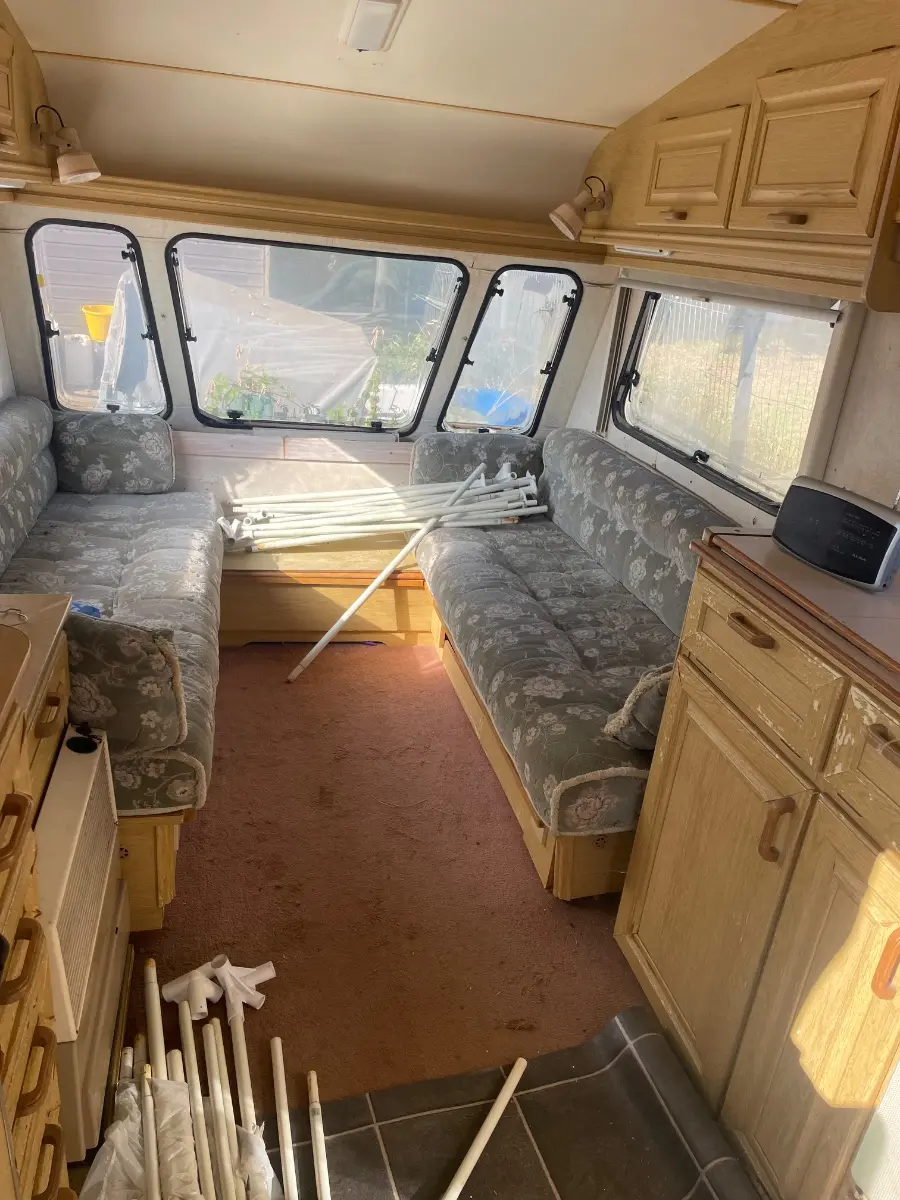 Caravan interior part-cleared with curtain poles and fittings stacked on the floor between the bench seats, what an owner is asked to sort before a collection date is set