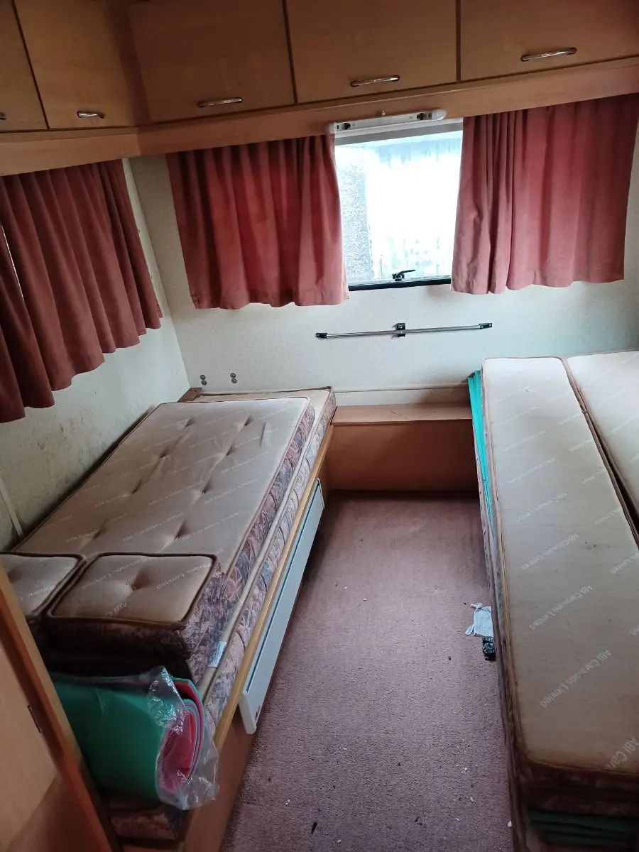 Twin-bed touring caravan interior with overhead lockers and curtains, dated but complete, the everyday condition our offers are built around